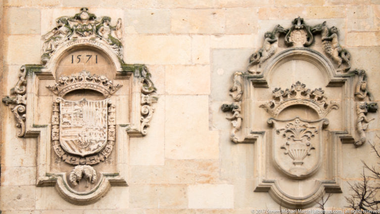 Two ornate carved stone coats of arms, one beneath the date 1571 and both framed by scrolling Renaissance-style ornament.