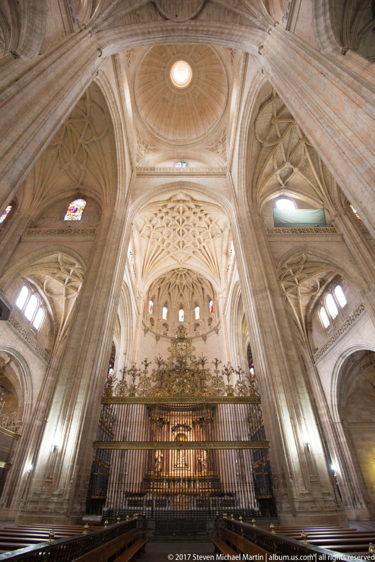 Wide interior view of Segovia Cathedral with clustered piers, elaborate ribbed vaults, stained glass, and a dark metal screen.