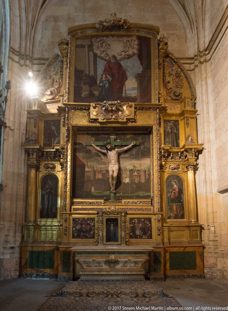 Large gilded cathedral retablo with central Crucifixion, surrounding painted panels, columns, and lower predella.