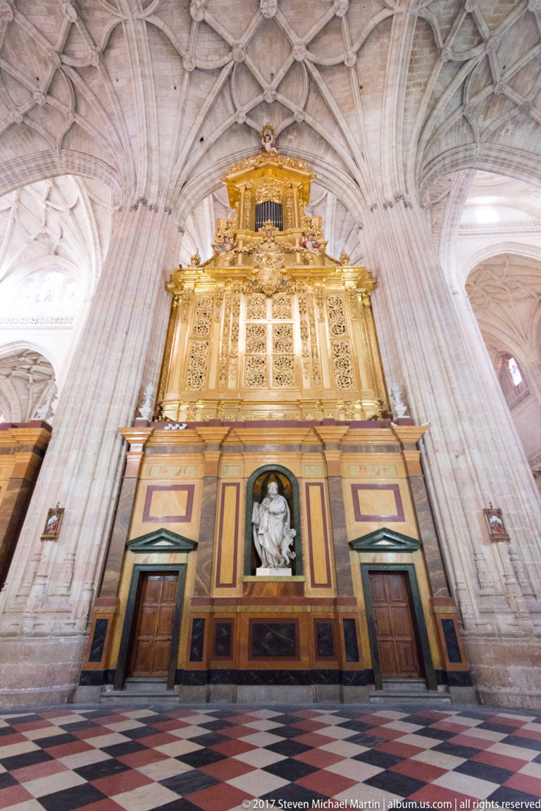 Tall polychrome and gilded chapel front beneath ribbed vaults, with central white devotional sculpture and paired doorways.
