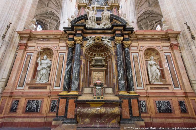 Polychrome cathedral altar with pink panels, dark marble columns, gilded capitals, central tabernacle, and white saint sculptures.