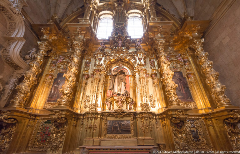 Large gilded cathedral retablo with central devotional figure, painted side panels, columns, scrollwork, and carved ornament.