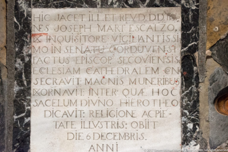 Close view of a rectangular stone memorial tablet carved with multiple lines of Latin capital lettering in a dark masonry surround.