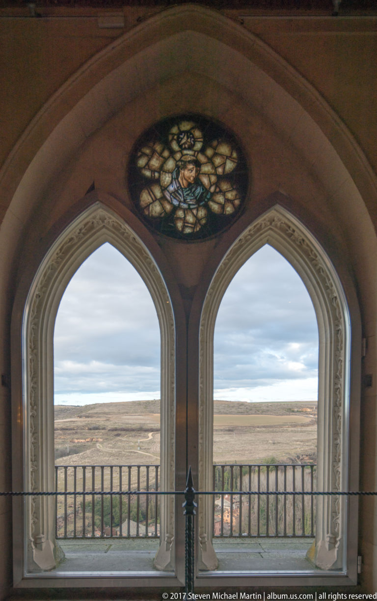 Two pointed-arch windows with carved surrounds overlook an open plateau, with a circular stained-glass medallion above.