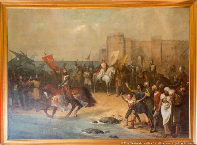 Framed historical painting with mounted and standing figures, banners, and a fortified city or castle in the background.
