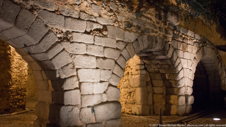 Close night view of massive stone arches built from large rough-cut blocks, with thick piers and strongly lit masonry joints.