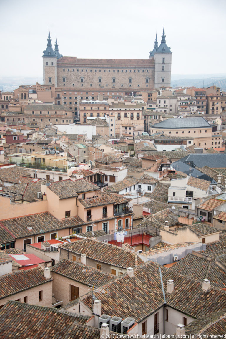 Historic Toledo rooftops filling the foreground with the Alcázar rising on the ridge beyond.
