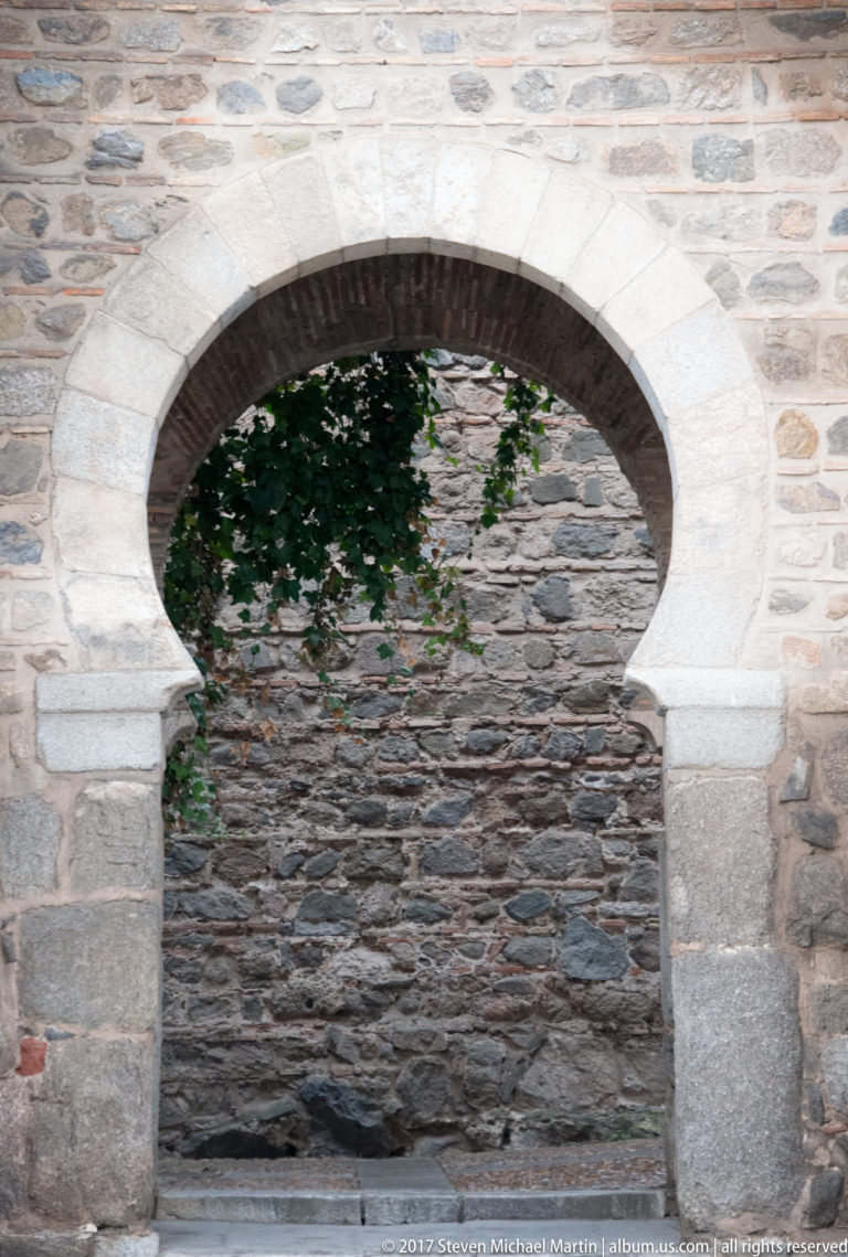 Large horseshoe-shaped arch with pale stone voussoirs set in an irregular masonry wall.