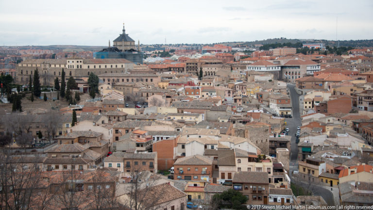 Elevated view across dense low-rise town roofs, streets, and a large historic complex in Castile-La Mancha.