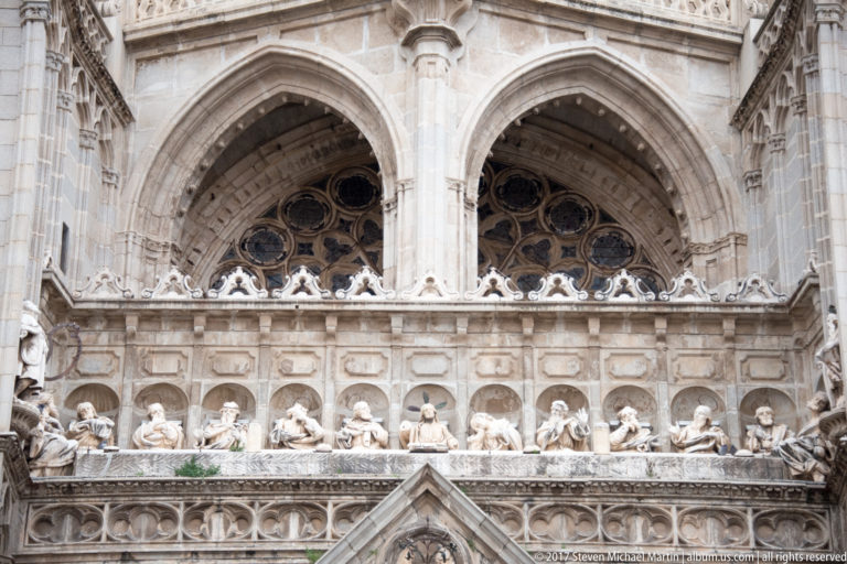 Close view of Toledo Cathedral with paired Gothic openings, tracery, and a horizontal row of carved figures in niches.