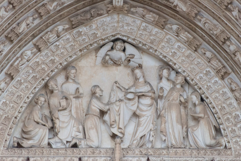 Close view of a Gothic tympanum relief with a central enthroned figure, surrounding attendants, and carved archivolts.