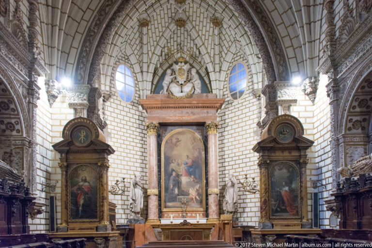 Symmetrical cathedral chapel with three devotional paintings set in carved stone architecture beneath a ribbed arch.