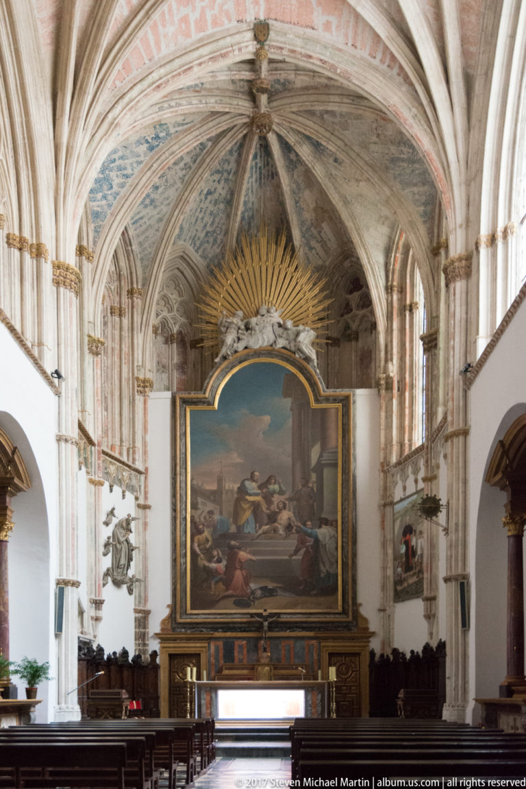Rib-vaulted cathedral chapel with a monumental religious painting above the altar and dark woodwork lining the lower walls.
