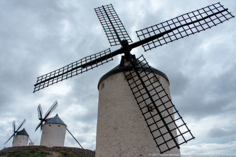 Low-angle view of a white tower windmill with large lattice sails, with two smaller windmills behind it.