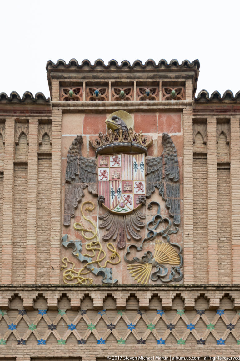 Polychrome royal coat of arms with a double-headed eagle mounted on a patterned brick façade.