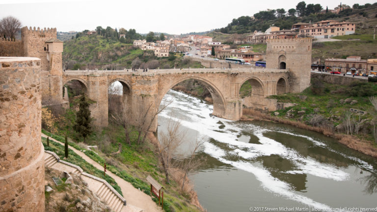 Puente de San Martín crossing the Tagus on a large pointed arch with smaller arches and a fortified tower at the far end.