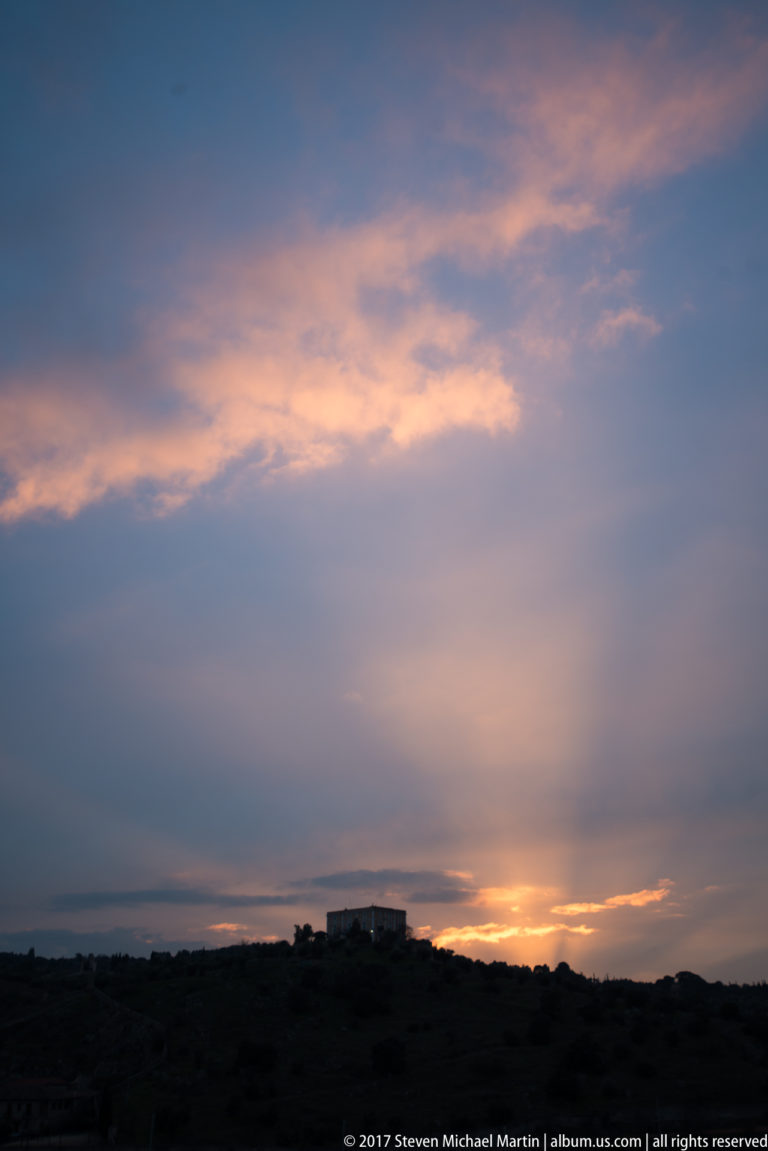 Orange sunset glow beneath layered blue-gray clouds above a dark low ridge outside Toledo.