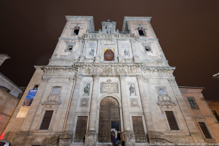 Illuminated Baroque façade of San Ildefonso with twin square towers, central doorway, sculpture niches, and stained glass.