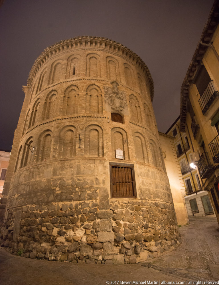 Large rounded brick church apse with tiers of blind arches above a rough stone base, illuminated at night.