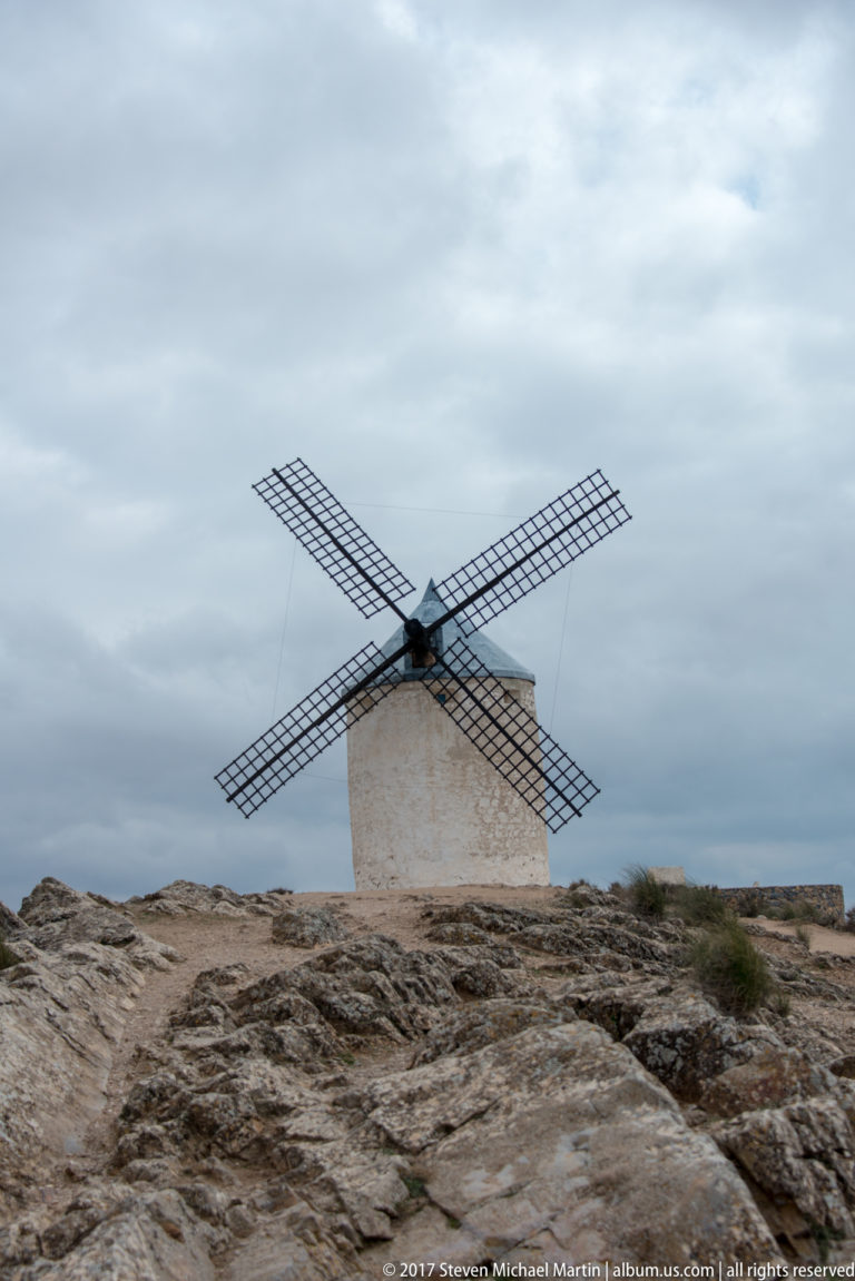 Single white tower windmill beyond a broad rocky limestone foreground under an overcast sky.
