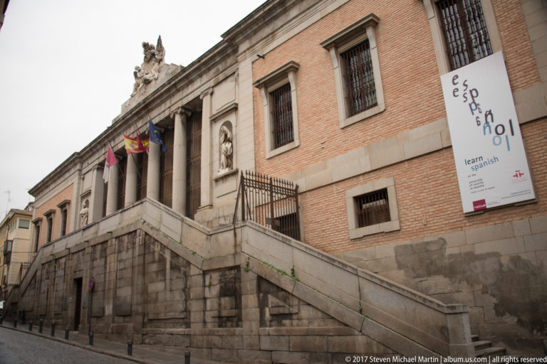 Brick-and-stone institutional building with exterior stairs, flags, barred windows, and a tall banner on the façade.