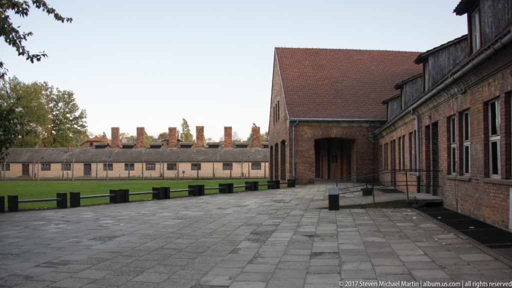 Red-brick and low stucco barracks border a broad paved courtyard with repeated chimneys at Auschwitz I.