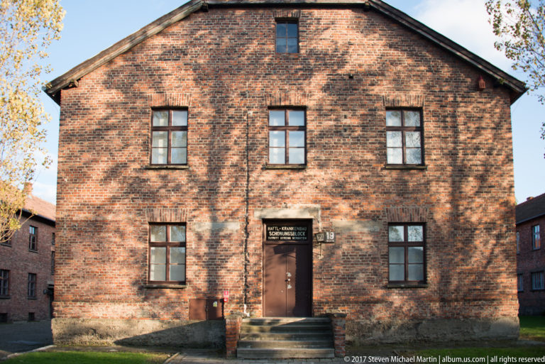Symmetrical red-brick façade of Auschwitz I Block 19 with central door, steps and evenly spaced windows.