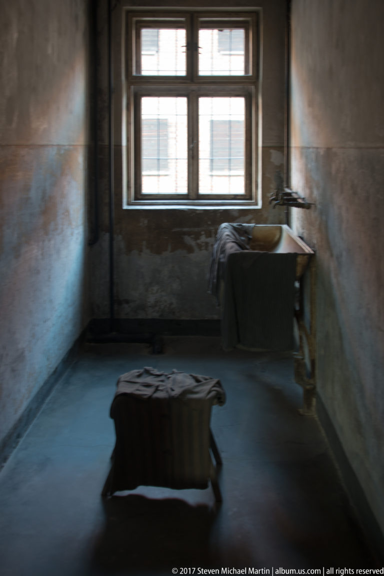 Bare room with a deep wash basin, exposed plumbing, window and low wooden fixture against stained plaster walls.
