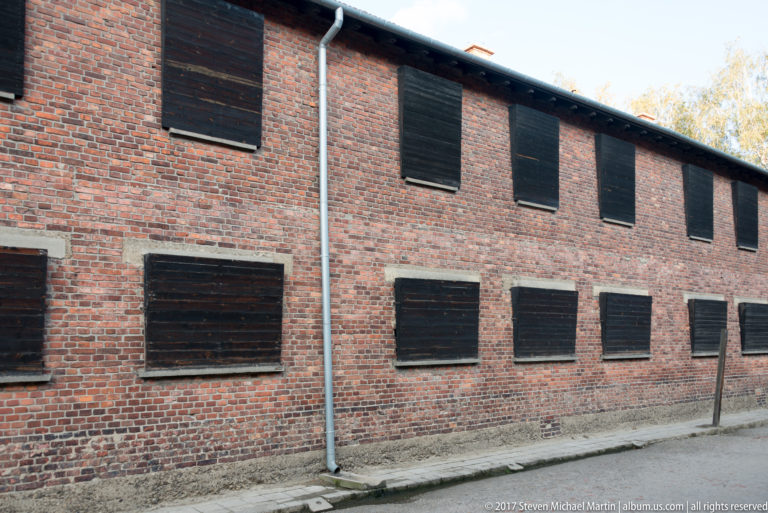 Long red-brick façade with rows of dark wooden shutters covering nearly every window opening.