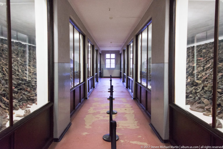 Long museum corridor with glass cases packed with shoes on both sides and queue posts down the center.