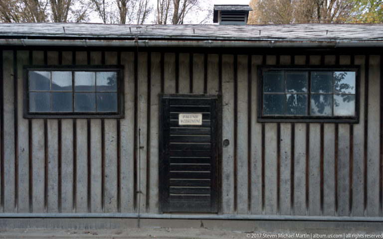 Weathered wooden façade with two multi-pane windows and a central door labeled “Prisoner Kitchen.”