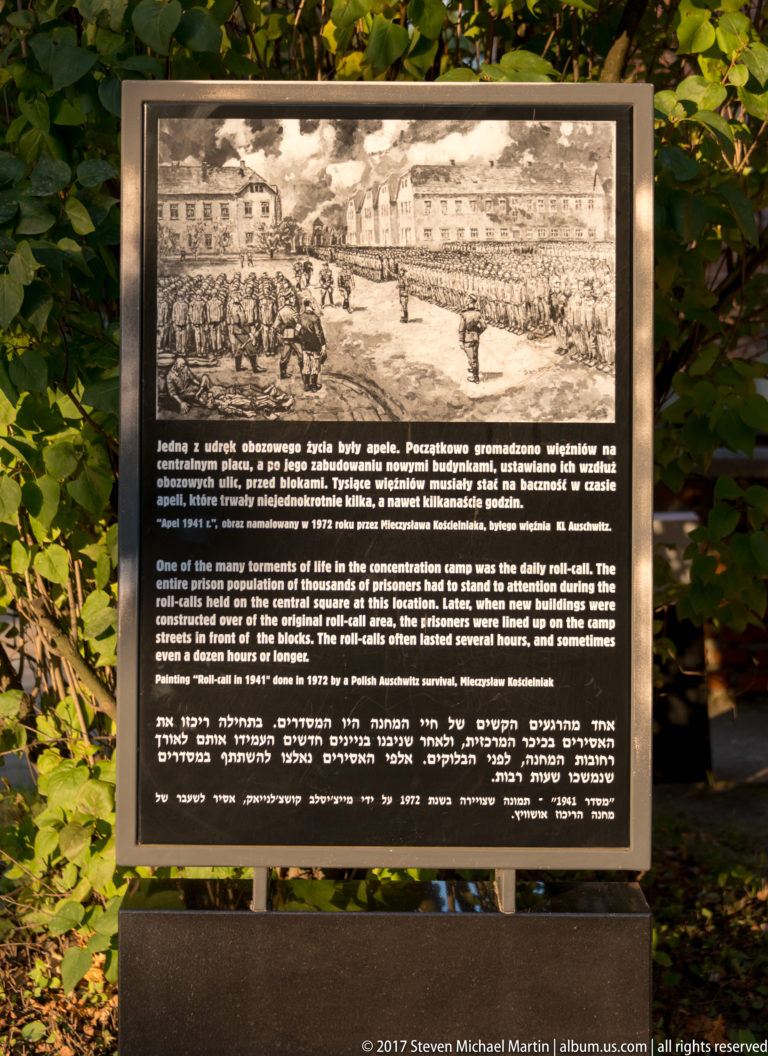 Outdoor multilingual panel with a historical drawing of Auschwitz barracks and explanatory text beneath.