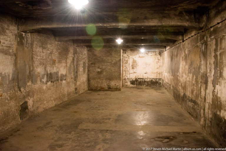 Bare gas-chamber interior with stained walls, concrete floor, low ceiling and overhead openings at Auschwitz I.