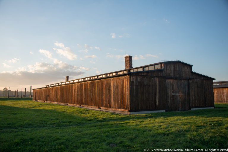 Long wooden barrack with brick chimney and raised roof ventilation structure at Auschwitz II-Birkenau.