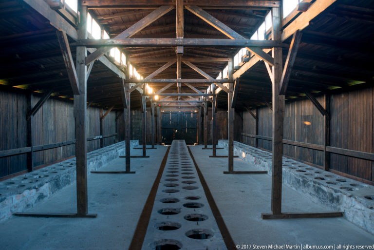 Communal barrack latrine with a long row of circular toilet openings beneath exposed timber framing.