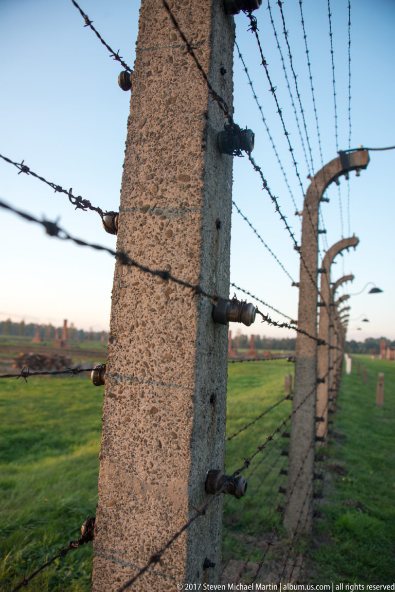 Close-up of a concrete perimeter post with ceramic insulators and multiple barbed-wire strands at Auschwitz II-Birkenau.