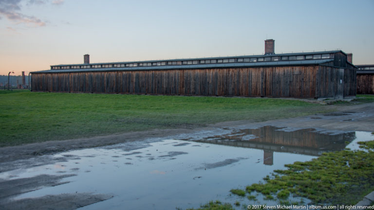Long wooden barrack reflected in a large puddle on the wet grounds of Auschwitz II-Birkenau.