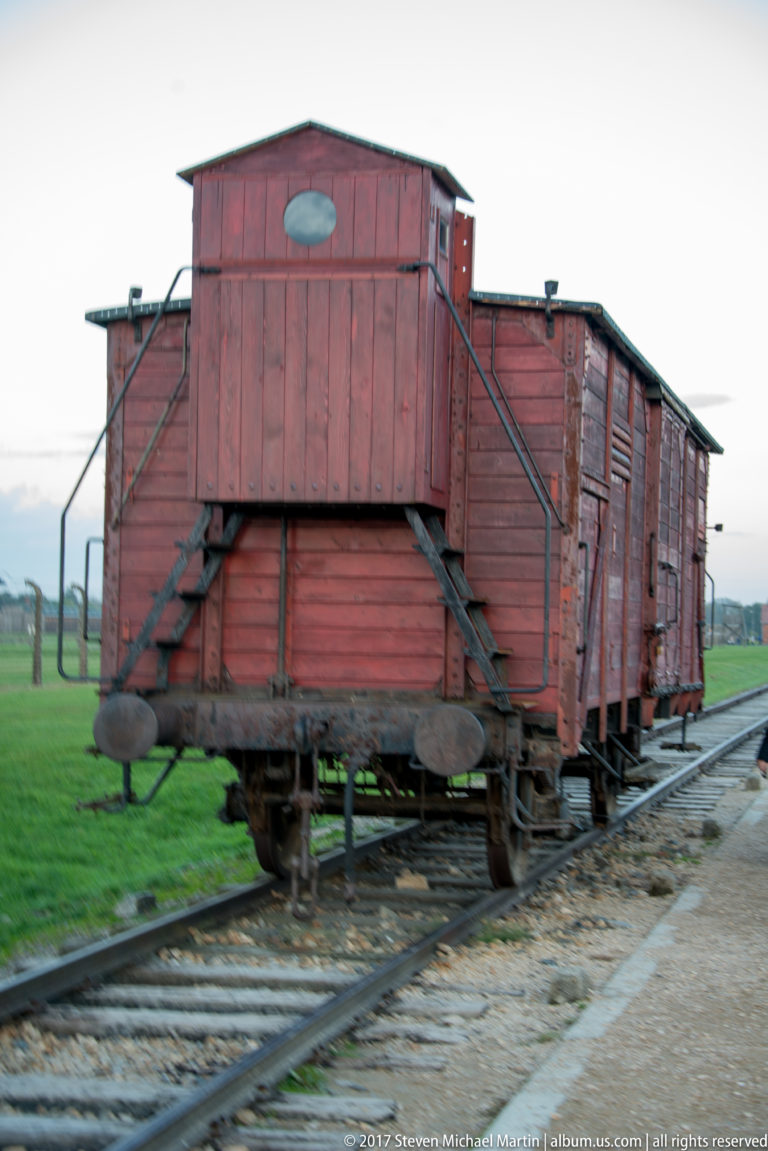 Weathered red wooden railway freight car standing on tracks at Auschwitz II-Birkenau.