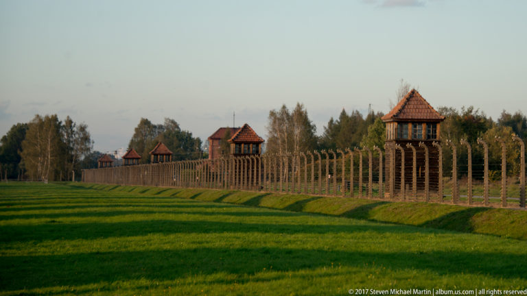 Several wooden guard towers aligned behind the barbed-wire perimeter fence at Auschwitz II-Birkenau.
