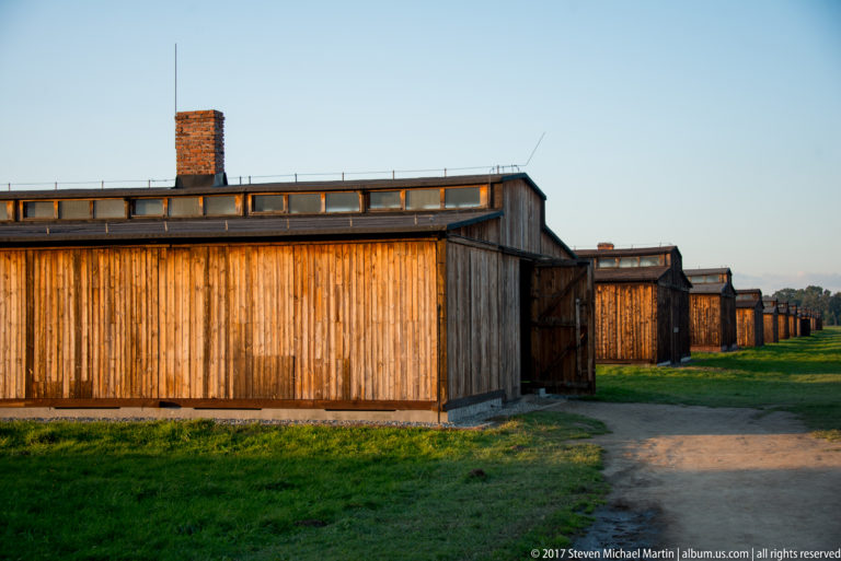 Wooden barrack with vertical plank walls and brick chimney, followed by similar barracks at Auschwitz II-Birkenau.