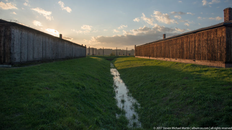 Water-filled drainage ditch running between two long wooden barracks at Auschwitz II-Birkenau.