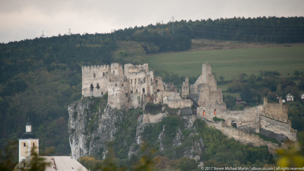 Ruined Beckov Castle crowns a steep limestone cliff above fields and village buildings in western Slovakia.