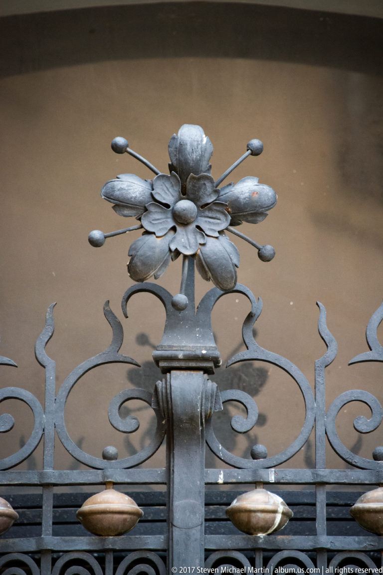 Stylized metal flower and curling wrought-iron scrollwork at the crest of a castle gate.