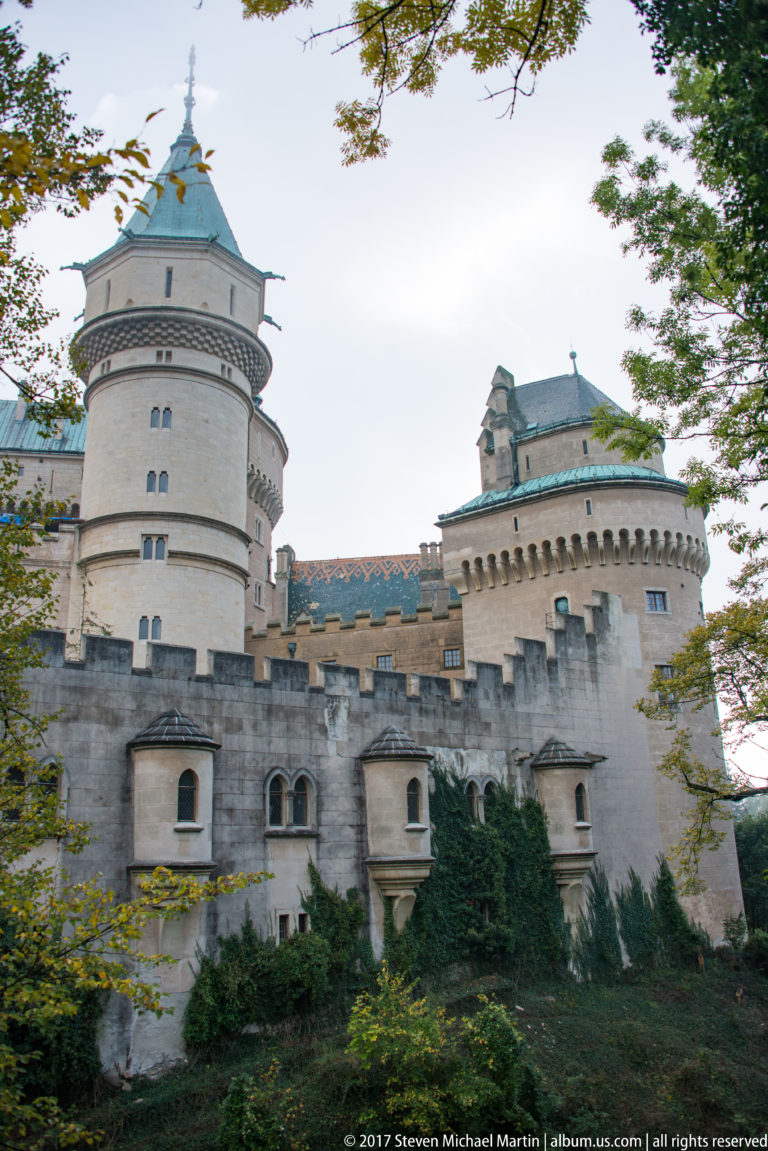 Round pale towers with steep roofs rise behind a crenellated wall at Bojnice Castle.