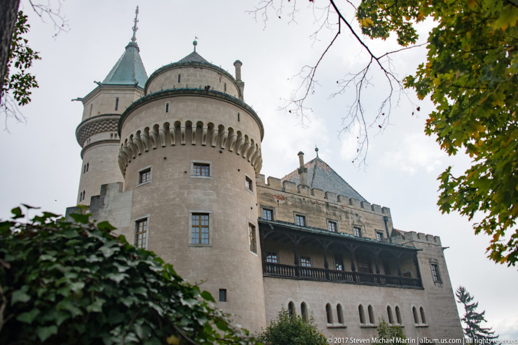 Round Bojnice Castle tower with corbelled upper wall beside a long dark timber gallery.