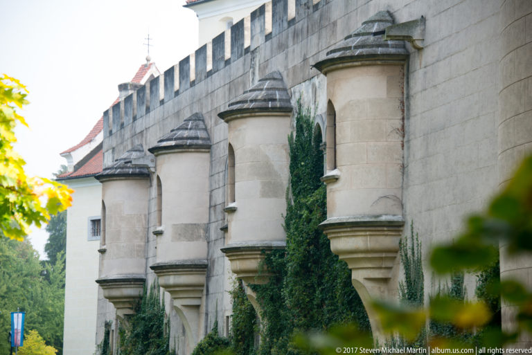 Three projecting stone bays repeat along a crenellated castle wall with ivy between them.