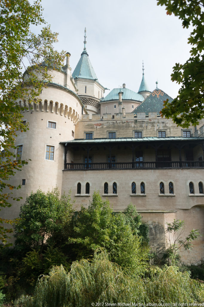 Bojnice Castle side elevation with dark timber gallery and steep-roofed towers above dense trees.