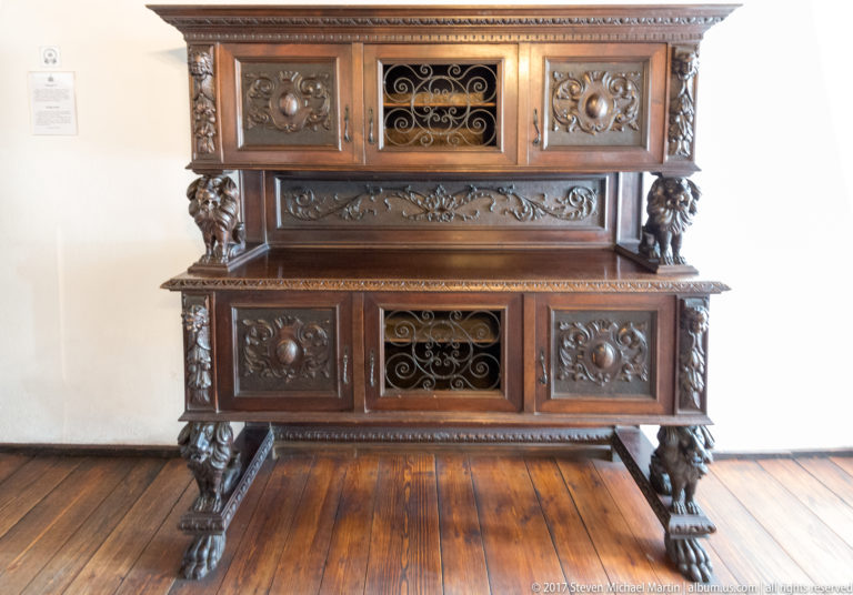Ornate two-part wooden cabinet with carved panels, metal grilles, and sculptural feet.