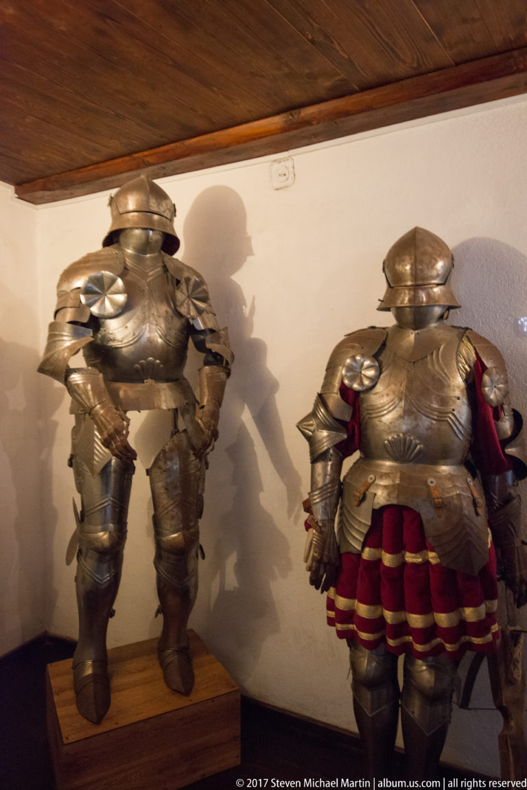 Two full suits of plate armor displayed side by side, one with red fabric visible beneath the metal plates.