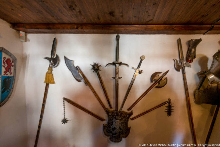 Wall-mounted display of swords, polearms, axes, and spiked weapons arranged in a fan pattern.